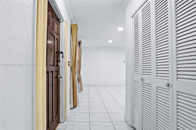 corridor with light tile patterned floors, a textured wall, ornamental molding, and recessed lighting