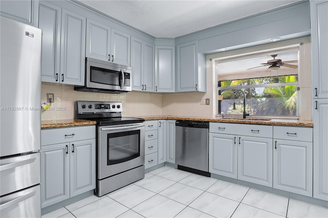 kitchen featuring decorative backsplash, ceiling fan, dark stone counters, a sink, and appliances with stainless steel finishes