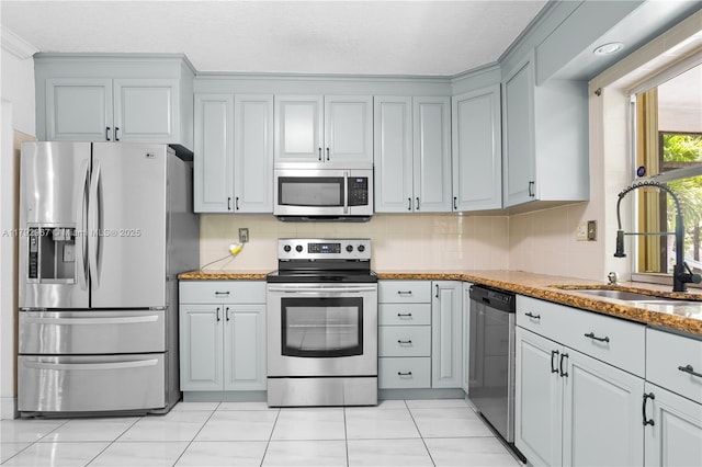 kitchen featuring decorative backsplash, light stone counters, a sink, appliances with stainless steel finishes, and light tile patterned floors