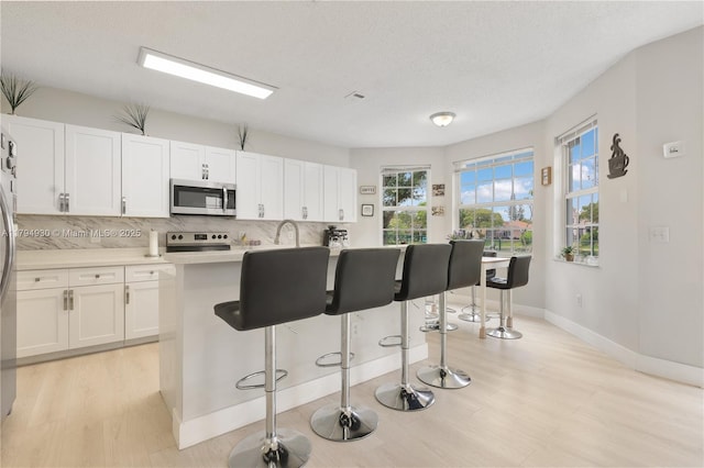 kitchen featuring white cabinets, light countertops, stainless steel appliances, baseboards, and decorative backsplash