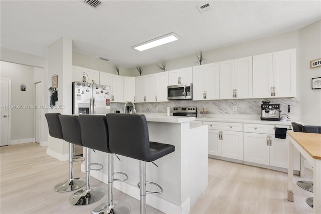 kitchen featuring appliances with stainless steel finishes, decorative backsplash, a breakfast bar area, and light wood finished floors