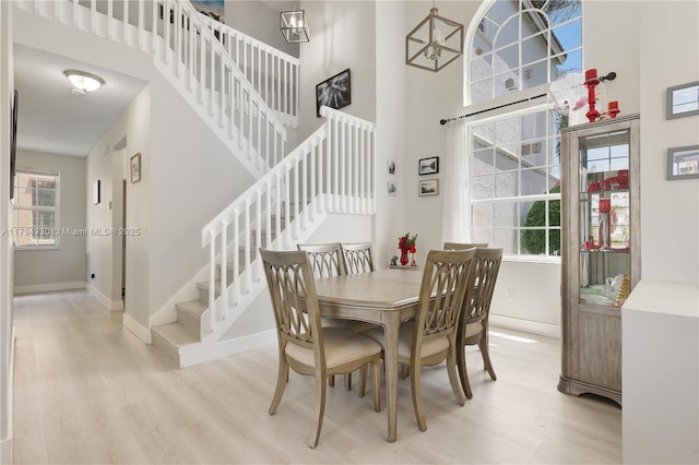 dining room featuring stairs, a high ceiling, baseboards, and light wood-style floors