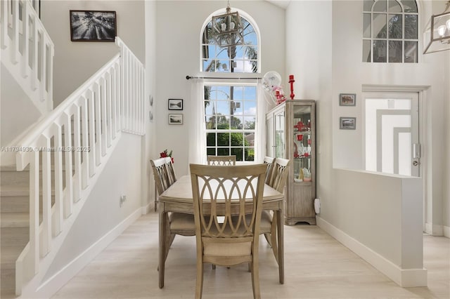 dining area with stairway, baseboards, a high ceiling, and light wood-type flooring