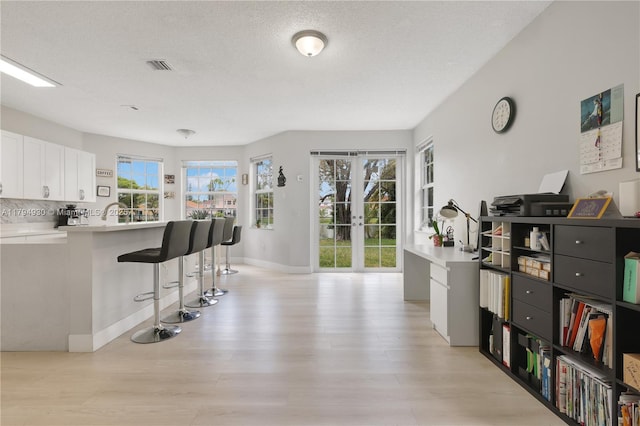 kitchen with a kitchen breakfast bar, visible vents, light countertops, white cabinets, and light wood-style flooring