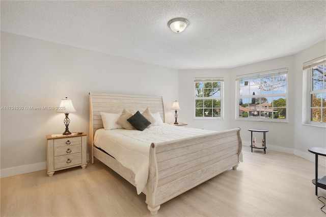 bedroom with baseboards, light wood finished floors, and a textured ceiling