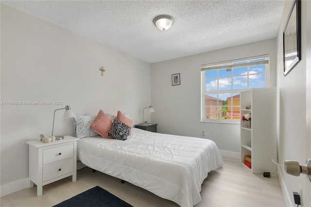 bedroom with baseboards, a textured ceiling, and light wood finished floors