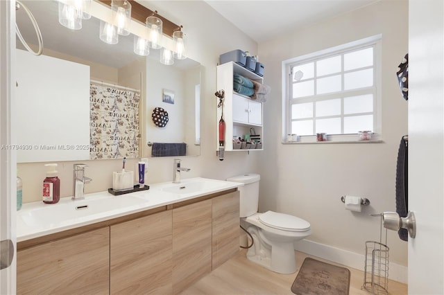 bathroom with double vanity, toilet, baseboards, and a sink