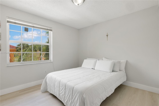 bedroom featuring baseboards, a textured ceiling, and wood finished floors