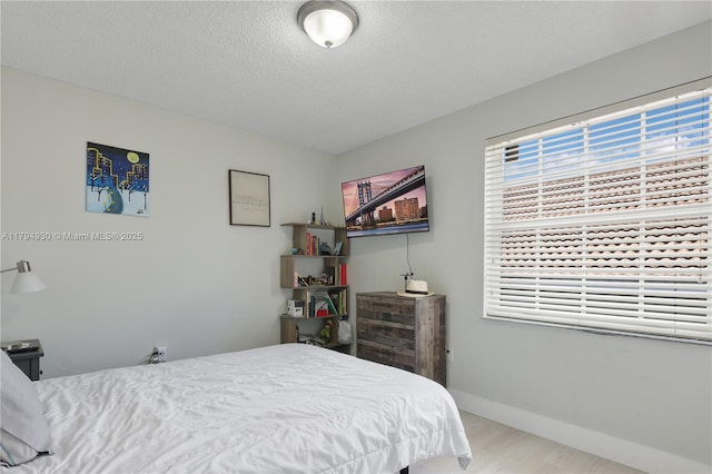bedroom featuring baseboards, a textured ceiling, and wood finished floors