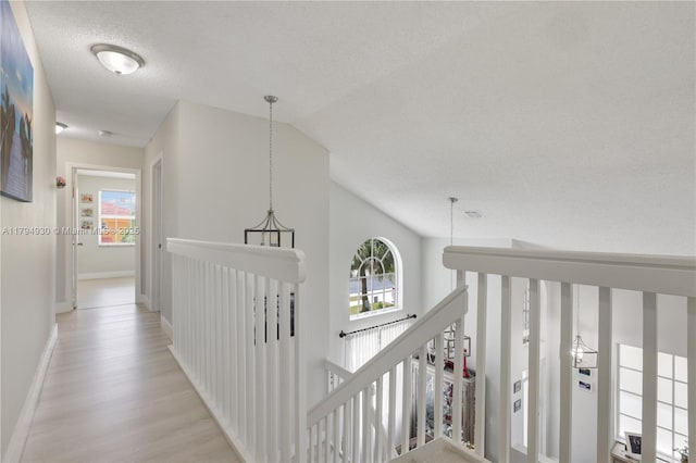 corridor featuring light wood-style floors, plenty of natural light, lofted ceiling, and an upstairs landing