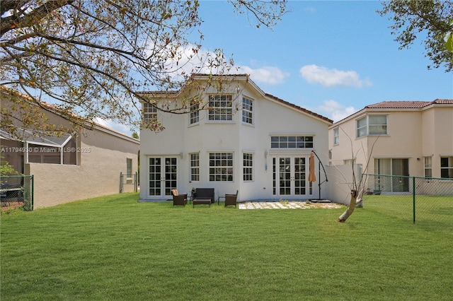 rear view of property featuring french doors, fence, stucco siding, and a yard
