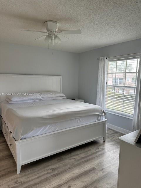 575 Augusta Blvd Unit 8, Naples, FL 34113 - bedroom featuring baseboards, a ceiling fan, a textured ceiling, and wood finished floors