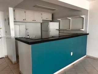 345 Ocean Dr Unit 904, Miami Beach, FL 33139 - kitchen with freestanding refrigerator, dark countertops, light tile patterned flooring, and white cabinetry