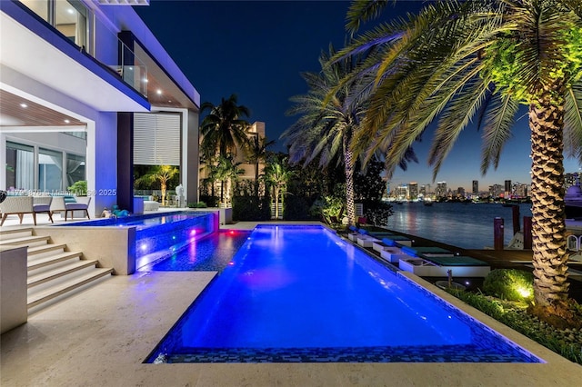 pool at night with a water view, a patio, and an outdoor pool