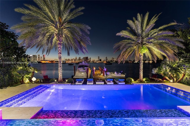 pool at night with a water view, a view of city lights, and an outdoor pool