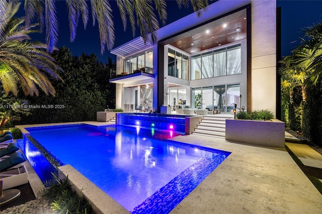 pool at twilight featuring a patio area, an outdoor pool, and a jacuzzi