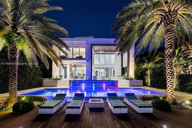 back of house at twilight featuring a deck, a jacuzzi, an outdoor pool, and stucco siding