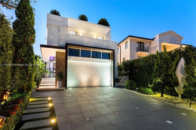 modern home with driveway, a garage, stucco siding, and a balcony
