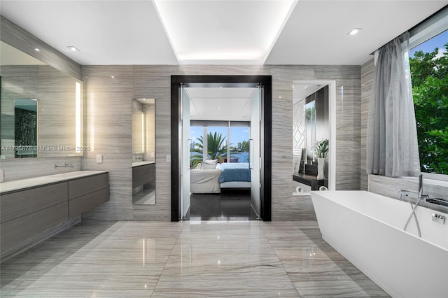 full bath with tile walls, ensuite bathroom, a freestanding tub, marble finish floor, and vanity