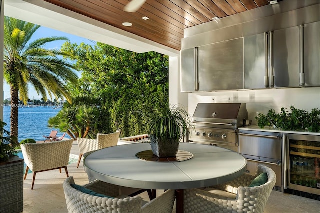 balcony featuring wine cooler, outdoor dining area, area for grilling, a patio, and a water view