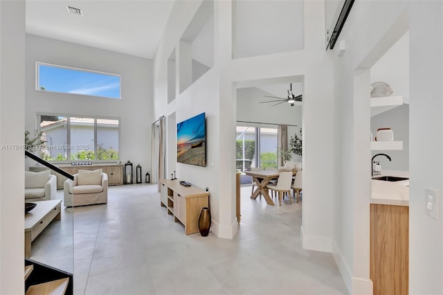 living area featuring a towering ceiling, baseboards, ceiling fan, and visible vents