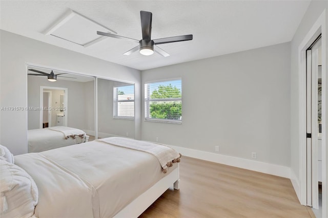 bedroom with ceiling fan, attic access, light wood-type flooring, baseboards, and a closet