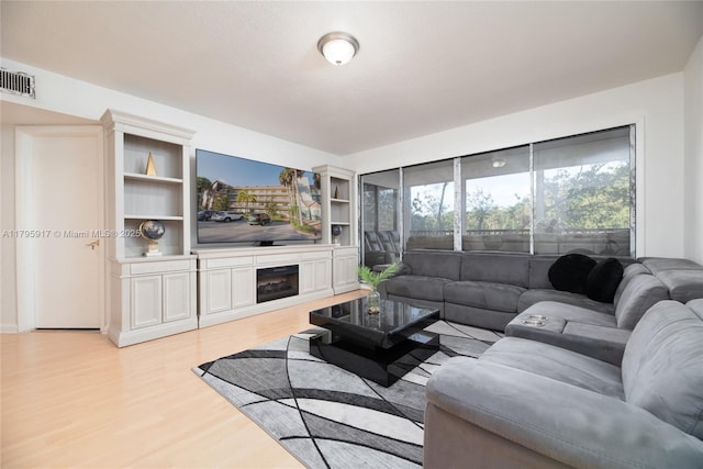 living room with visible vents, light wood-style flooring, and a glass covered fireplace