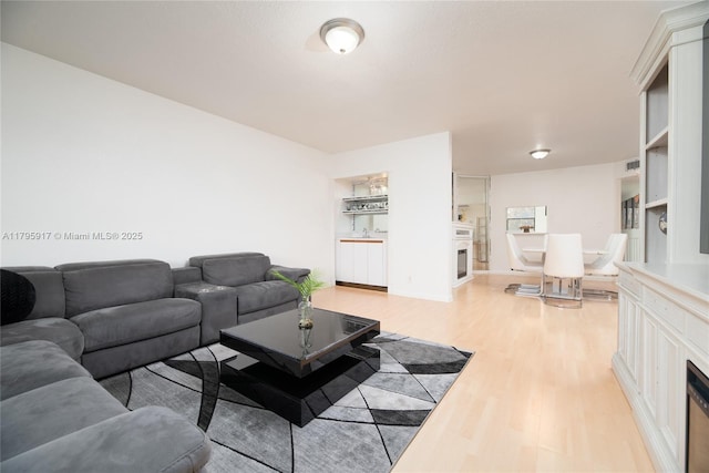 living area with a fireplace, light wood-type flooring, and visible vents