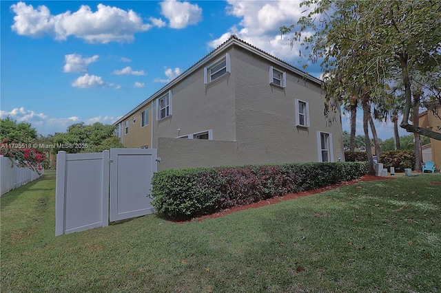 view of property exterior featuring fence, a gate, stucco siding, and a lawn