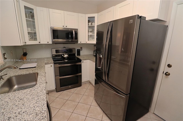 kitchen featuring white cabinetry, tasteful backsplash, light stone counters, a sink, and stainless steel appliances