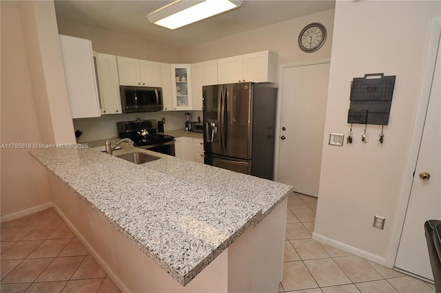 kitchen featuring a peninsula, glass insert cabinets, a sink, light tile patterned floors, and stainless steel appliances