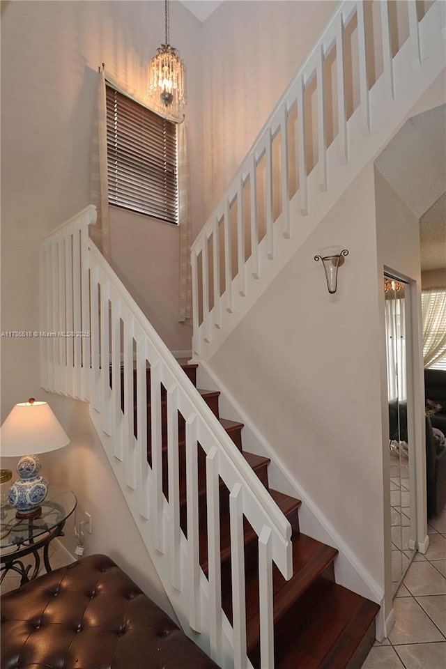 stairway featuring tile patterned flooring, a towering ceiling, and a notable chandelier