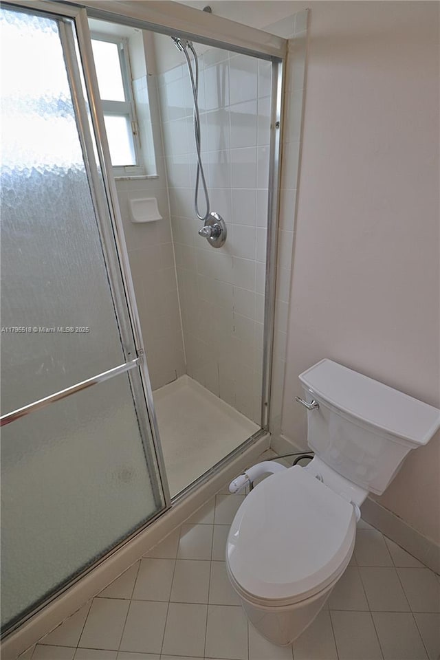 bathroom with toilet, tile patterned floors, baseboards, and a stall shower