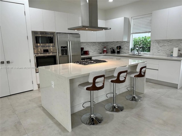 kitchen featuring decorative backsplash, island range hood, appliances with stainless steel finishes, a center island, and a sink