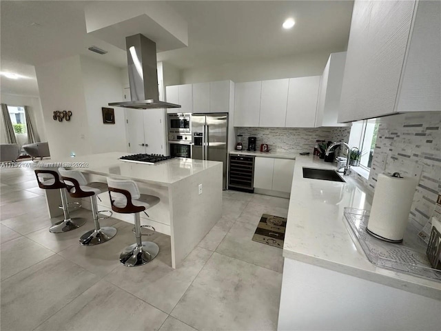 kitchen with a breakfast bar, beverage cooler, island range hood, a sink, and appliances with stainless steel finishes