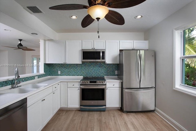 kitchen featuring appliances with stainless steel finishes, a sink, a ceiling fan, decorative backsplash, and visible vents