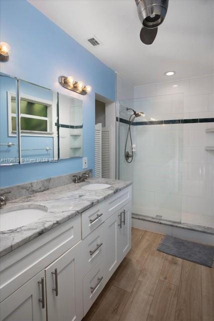 bathroom featuring double vanity, a tile shower, a sink, and wood finished floors