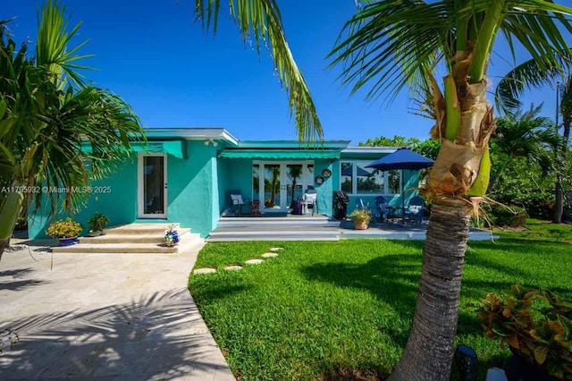 rear view of house with french doors, stucco siding, and a yard