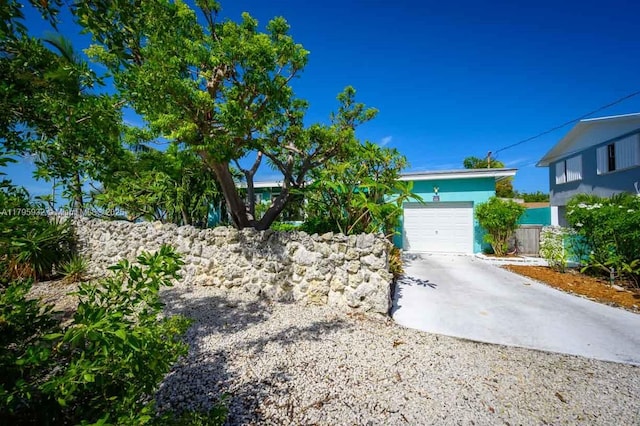 view of property hidden behind natural elements featuring a garage and concrete driveway