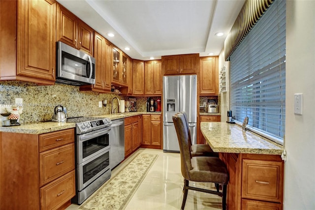 kitchen featuring light stone countertops, appliances with stainless steel finishes, a breakfast bar area, recessed lighting, and backsplash