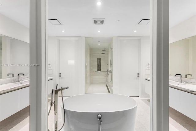 bathroom with visible vents, a freestanding tub, two vanities, and a shower stall