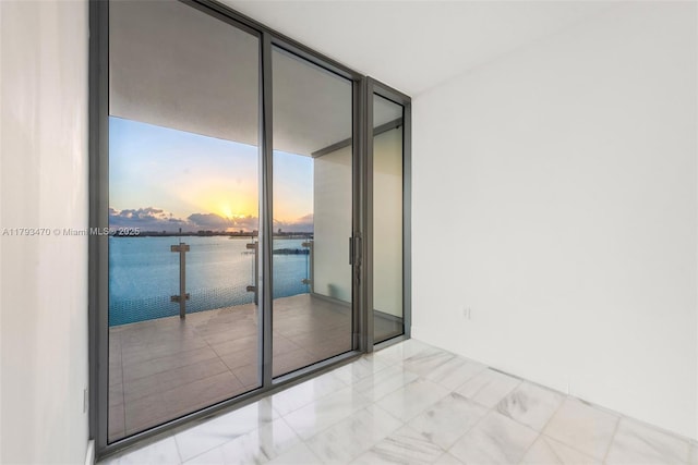 spare room featuring marble finish floor, a water view, and a wall of windows