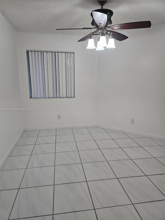 empty room with a textured ceiling, ceiling fan, light tile patterned flooring, and baseboards