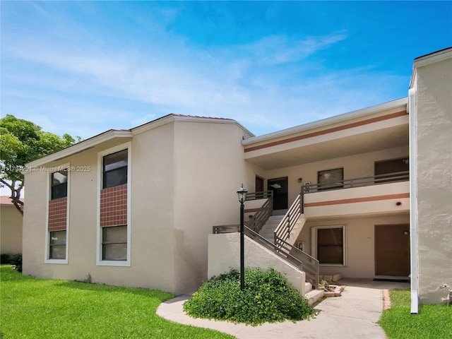 view of front of property with stairs, a front lawn, and stucco siding