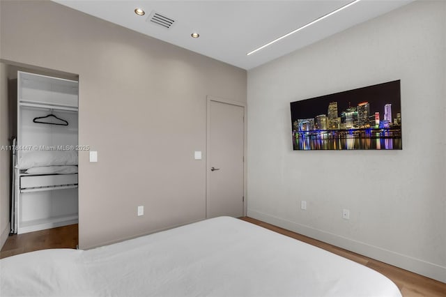 bedroom with a spacious closet, baseboards, wood finished floors, and visible vents