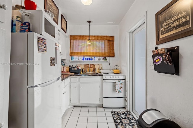 kitchen with dark countertops, white appliances, white cabinets, a sink, and light tile patterned floors