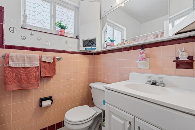 bathroom featuring vanity, a wainscoted wall, toilet, and tile walls
