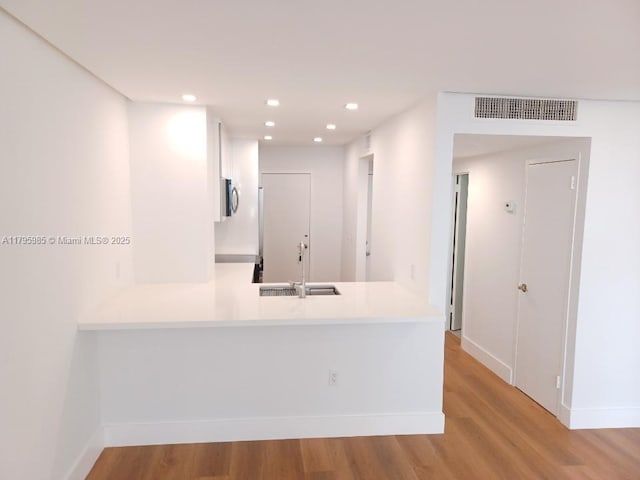 kitchen featuring a sink, light wood finished floors, light countertops, a peninsula, and visible vents