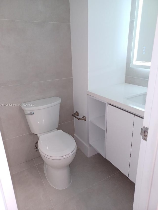half bath featuring toilet, tile patterned floors, tile walls, and vanity