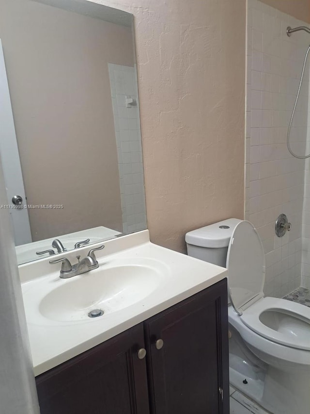 full bath featuring a textured wall, toilet, and tiled shower